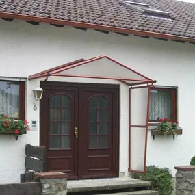 Eingangsbereich eines Einfamilienhauses mit Doppeltür, Vordach und Blumen am Fenster.