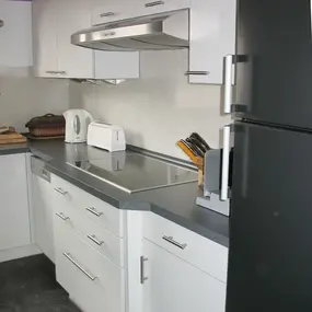 Moderne Einbauküche mit weißen Schränken, Elektrogeräten und grauer Arbeitsplatte.