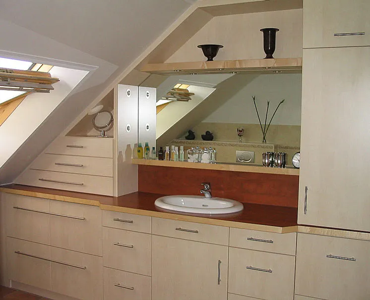Modernes Badezimmer mit Dachschräge, großem Spiegel, Waschbecken und hellen Einbauschränken.